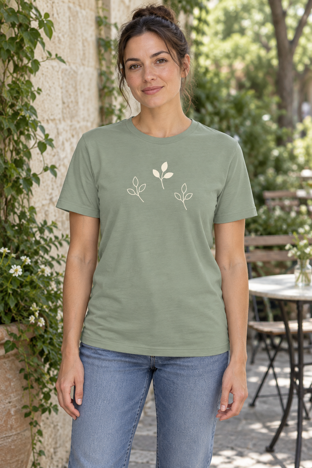 AI image of a fictional adult wearing the Sage Branch Study tee with three cream sprigs across the front in a garden café.